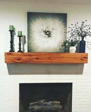 Red cedar mantle with decor, featuring candlesticks and artwork, installed above a white brick fireplace.