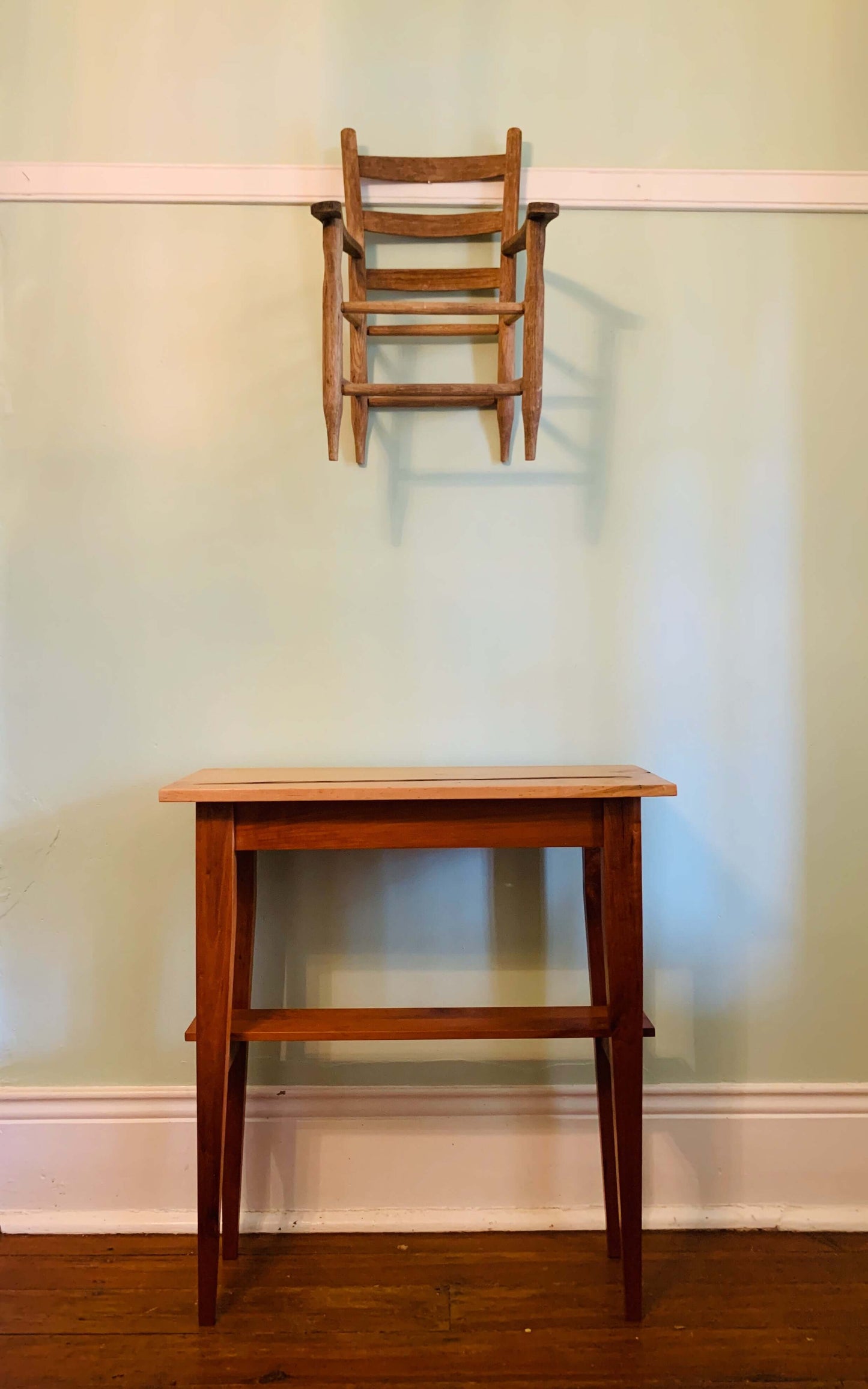 Elegant wooden hall table against a light green wall with a decorative chair piece hanging above.