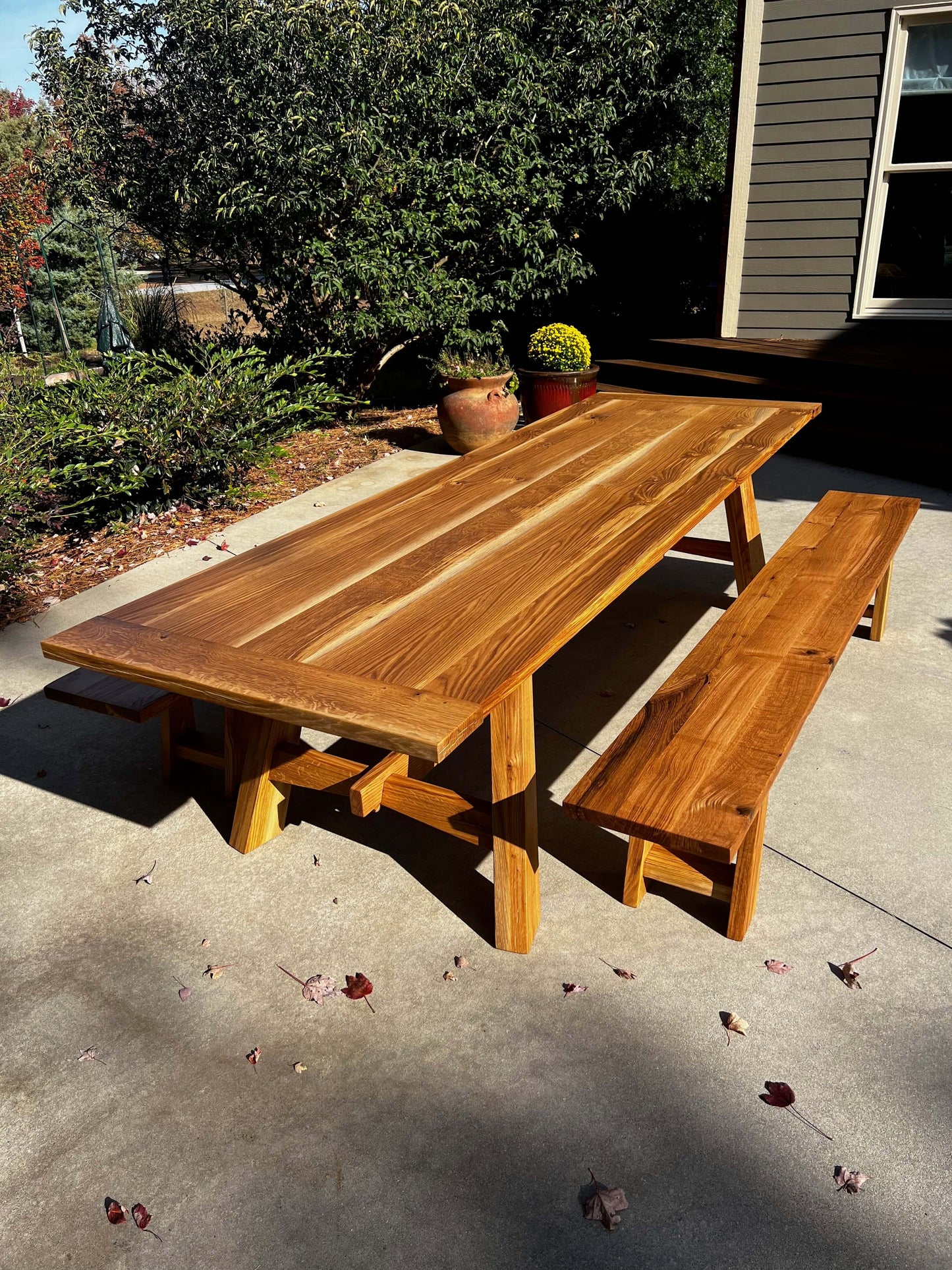 Elegant wooden dining table with matching bench, set outdoors, showcasing natural sunlight-inspired design elements.