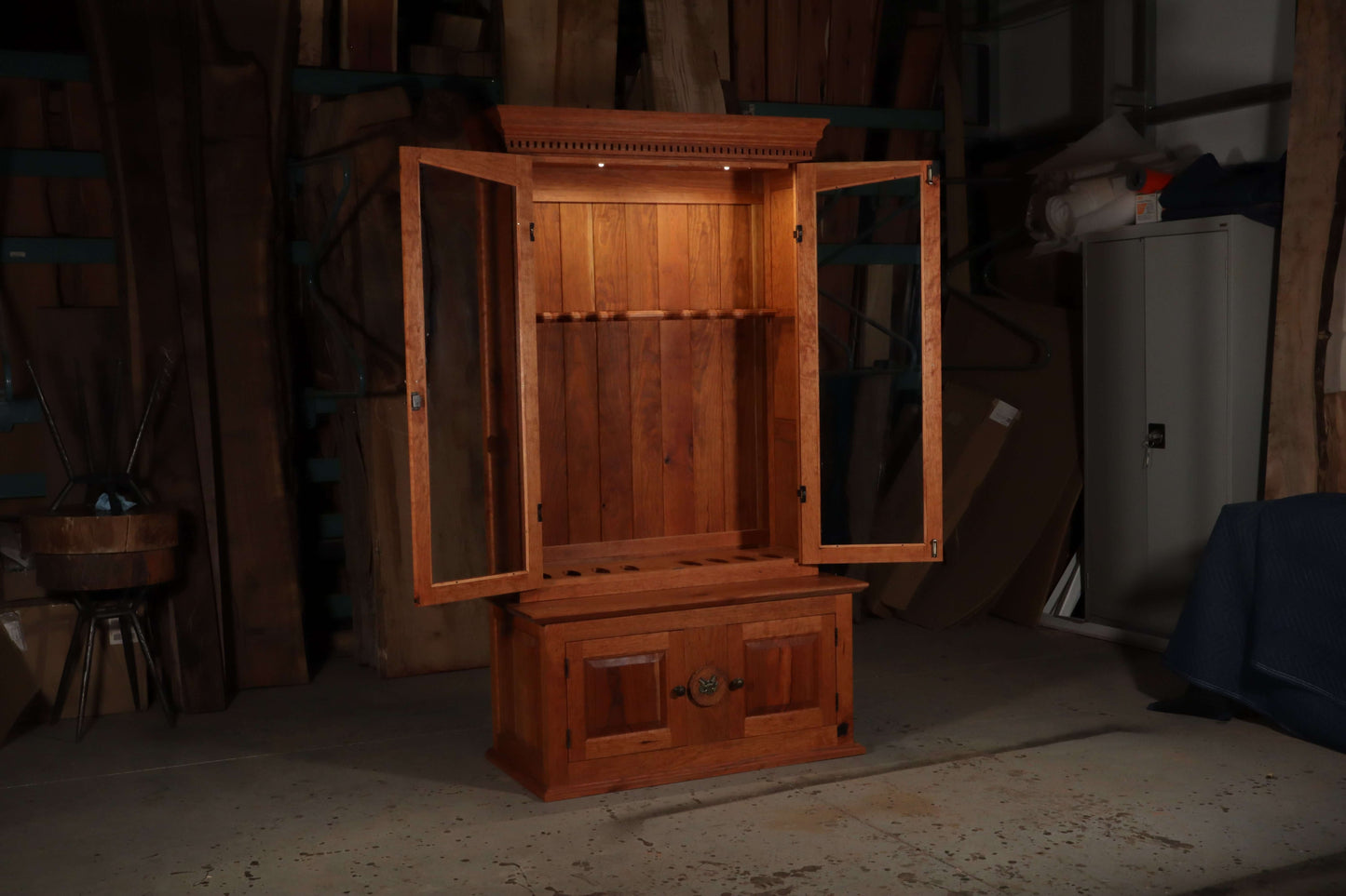 Solid wood gun case in cherry with open lockable upper rack and lower cabinets for elegant home or office storage.