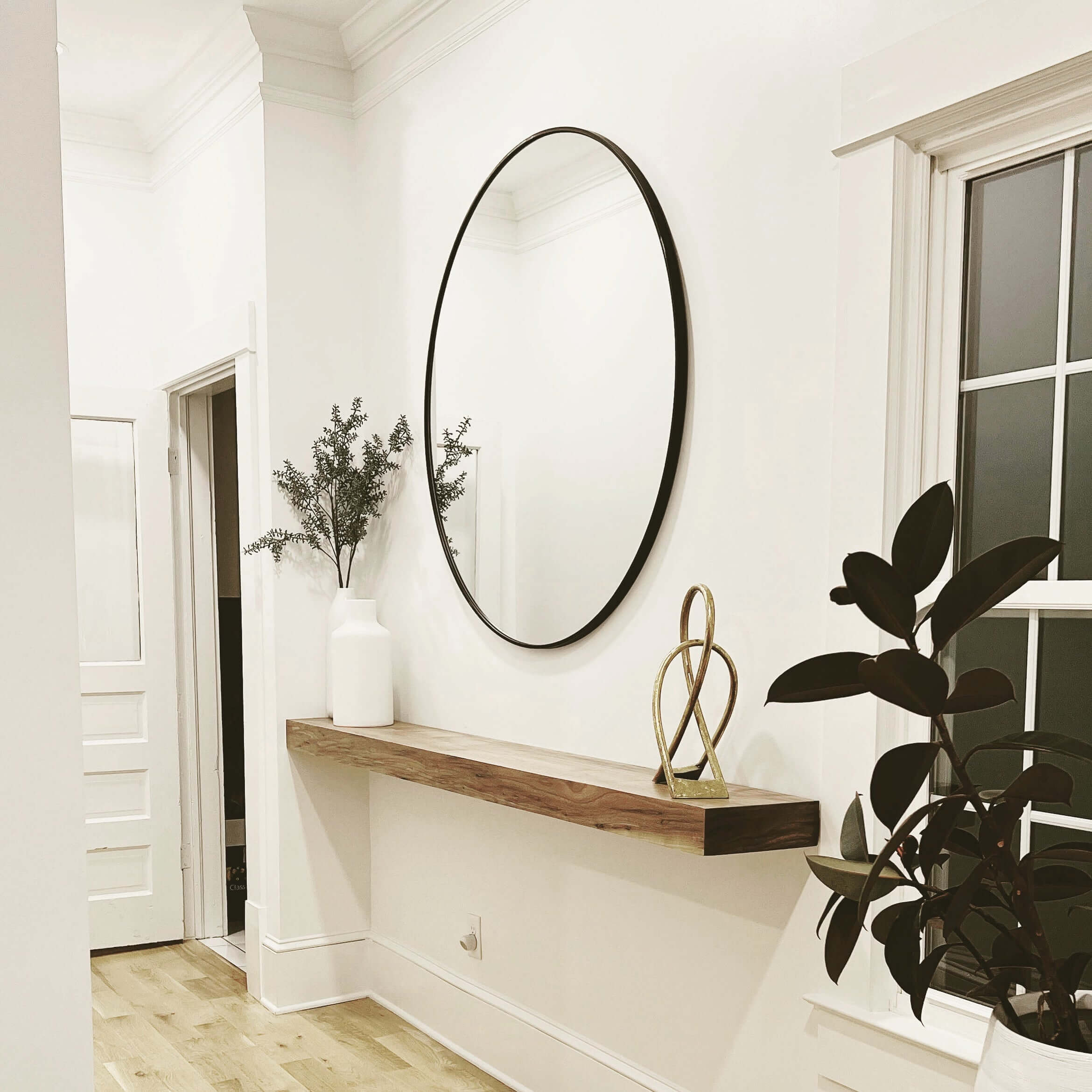Modern hallway with faux beam mantle, round mirror, and decorative plants.
