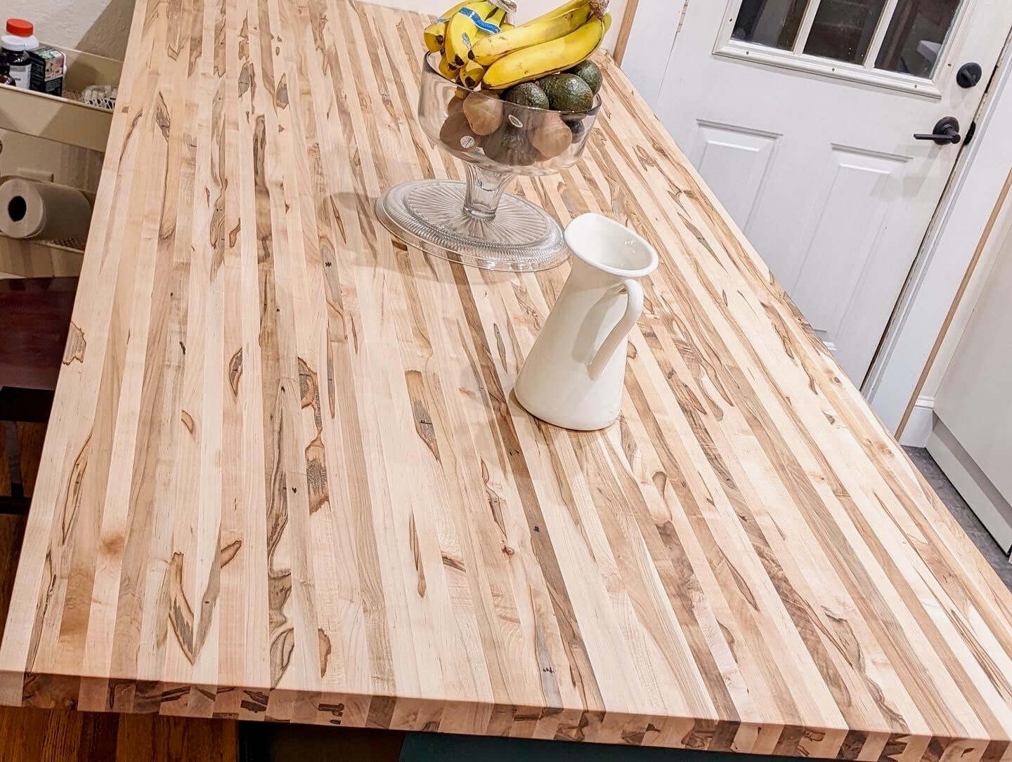 Butcher block countertop with natural hardwood patterns, featuring a fruit bowl and white pitcher, adding elegance to a kitchen space.