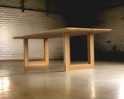 Modern wood dining table with U-shaped trestle base, The Bonita, showcasing sleek design and solid wood construction in a contemporary setting.