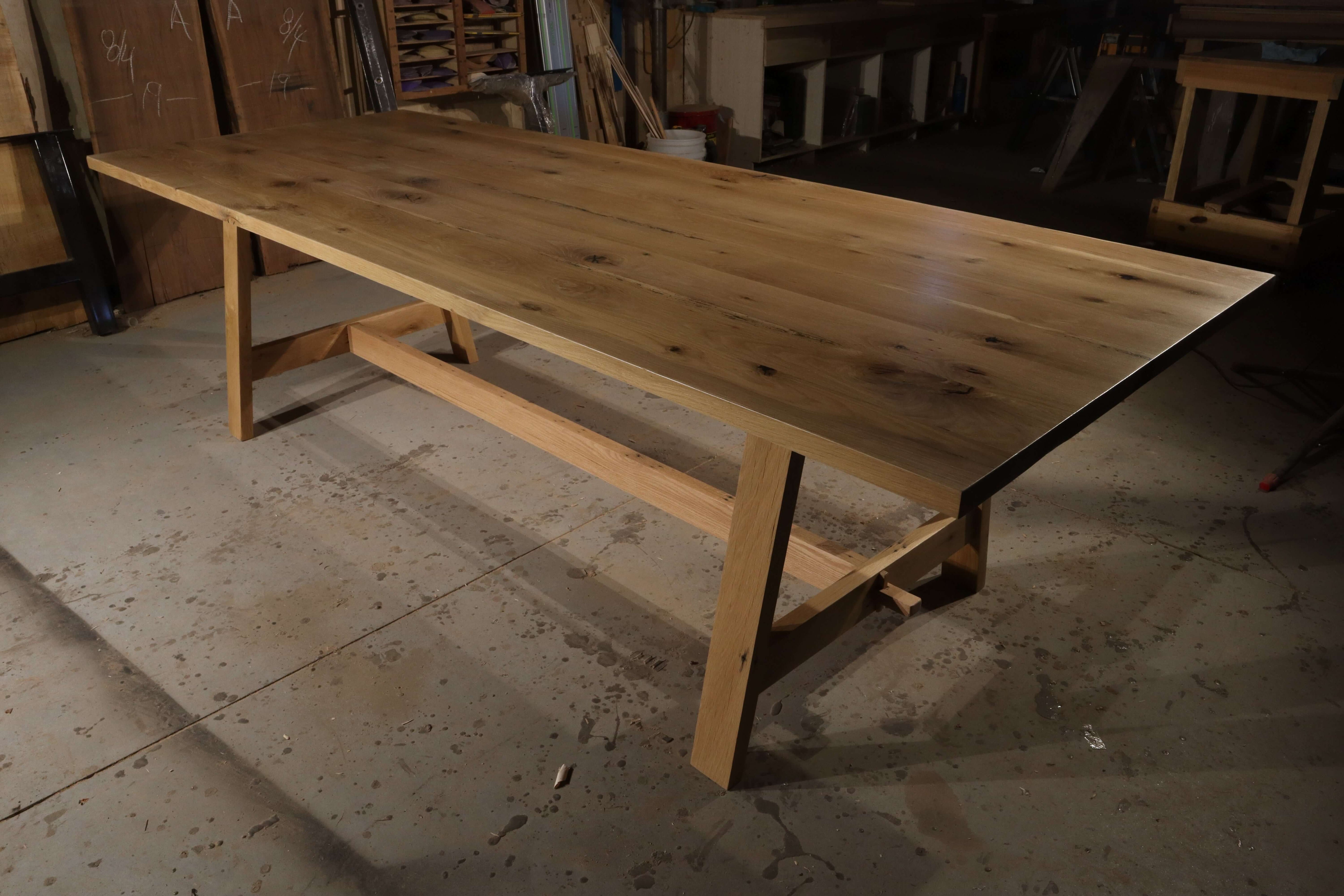 Rustic solid wood farmhouse trestle table in workshop, embodying timeless elegance and durability for gatherings.