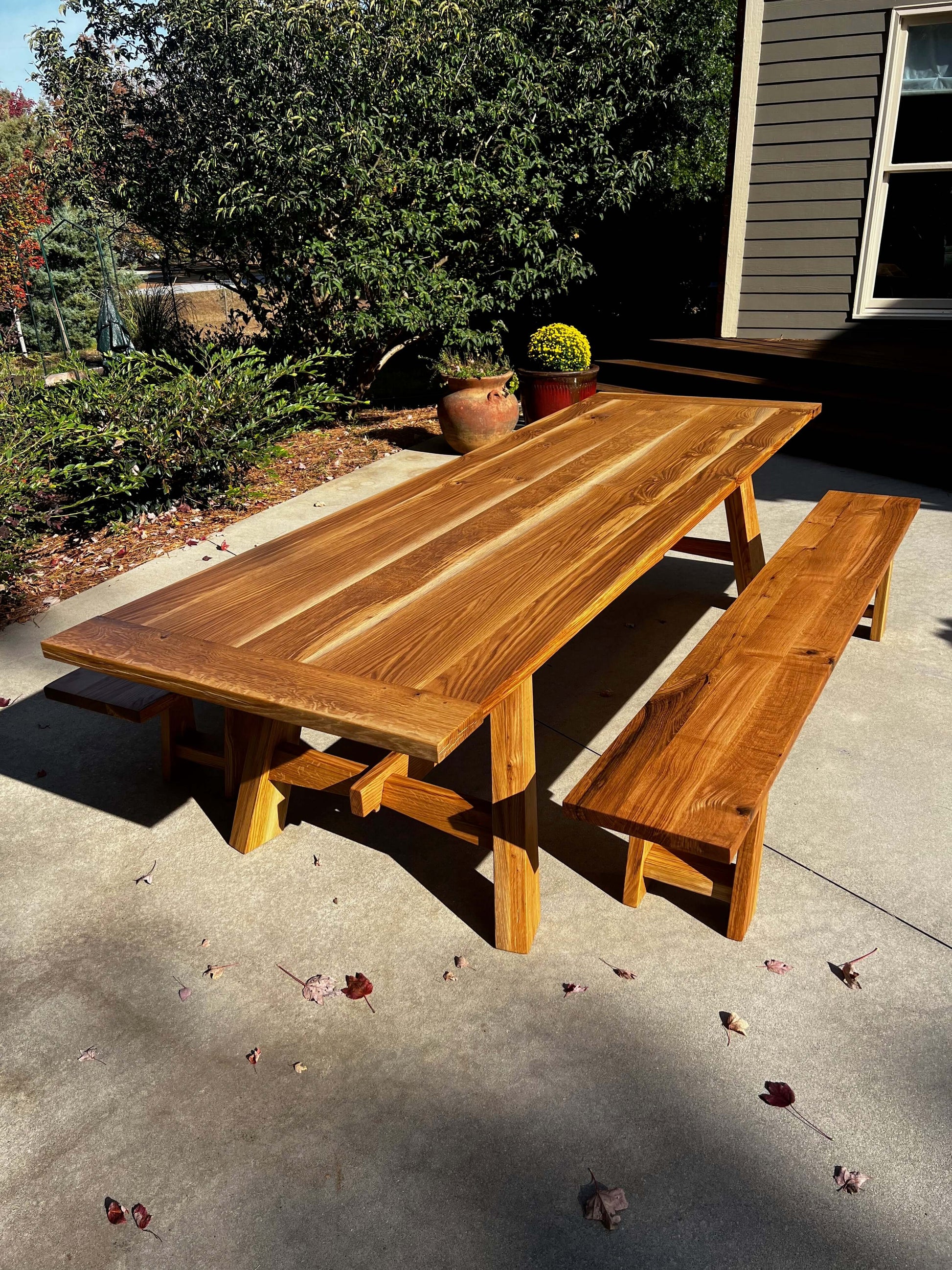 Elegant wooden dining table with matching bench, set outdoors, showcasing natural sunlight-inspired design elements.