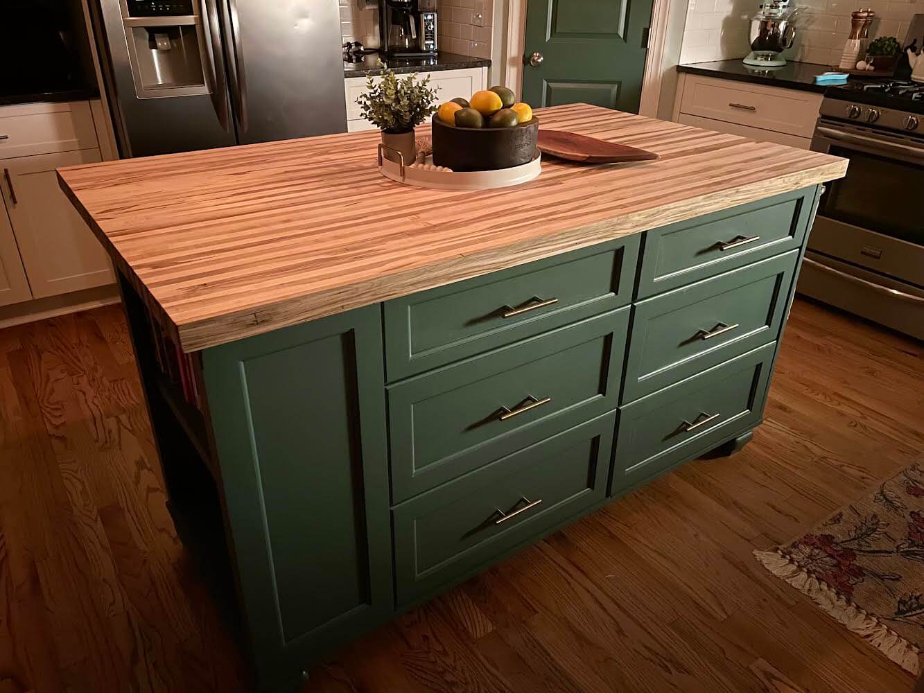 Elegant kitchen island with a butcher block countertop, showcasing rich hardwood textures and a sophisticated design with green cabinets.