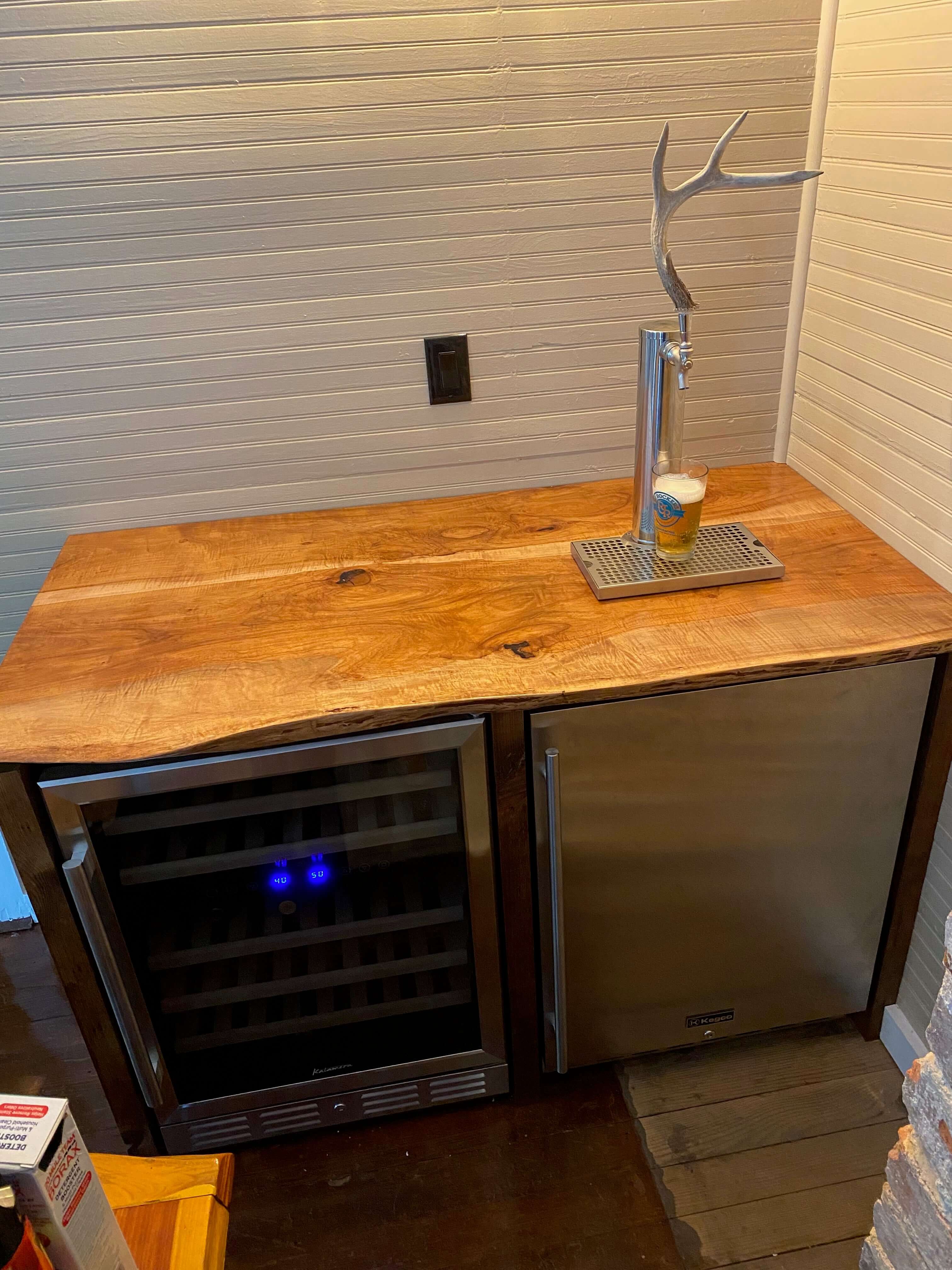Rustic live edge wood countertop with antler beer tap and built-in wine cooler in a modern kitchen setting.