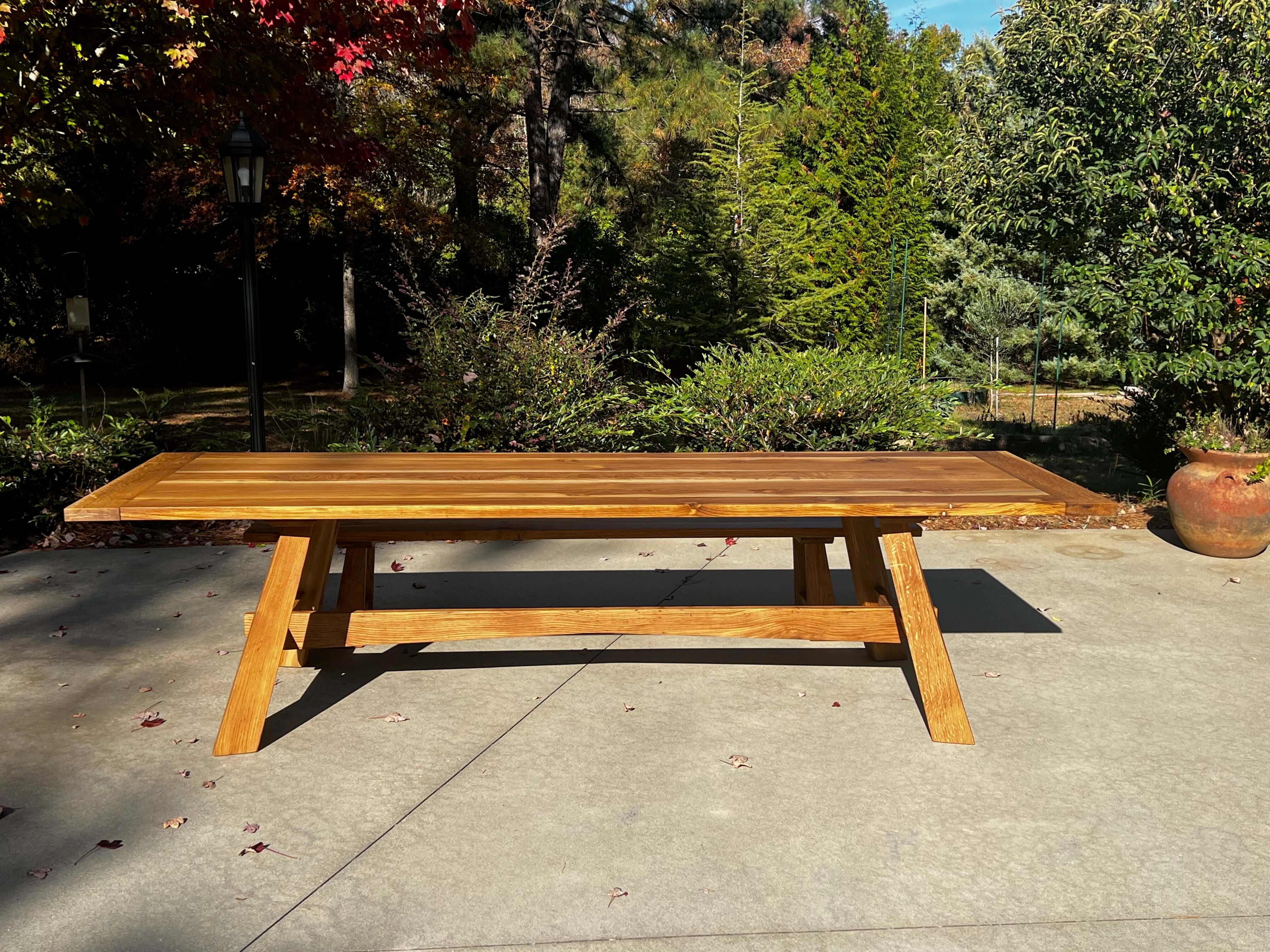 The Nikko Dining Table in sunlight with Japanese-inspired design, reflecting sun rays on a patio with lush greenery in the background.