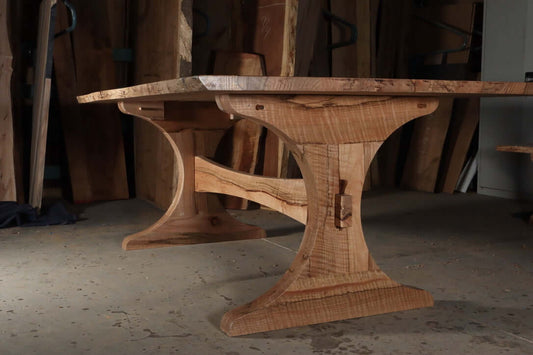Rustic solid wood trestle dining table with unique curved design, customizable in size and wood species for a lasting family statement piece.